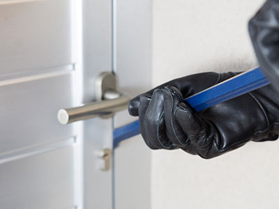 Eine Hand in einem schwarzen Handschuh, die ein blaues Werkzeug gegen eine Tür hält.