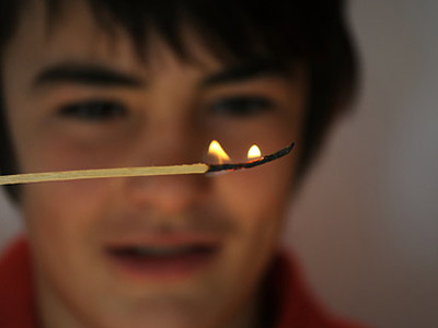 Ein Junge hält einen angezündeten Streichholz und schaut fasziniert darauf.